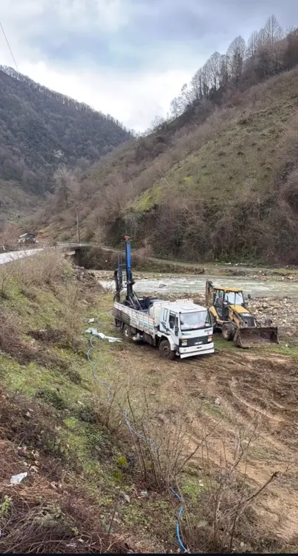 Dağlık vadi tabanında dere kenarında sondaj aracı ve iş makinesi